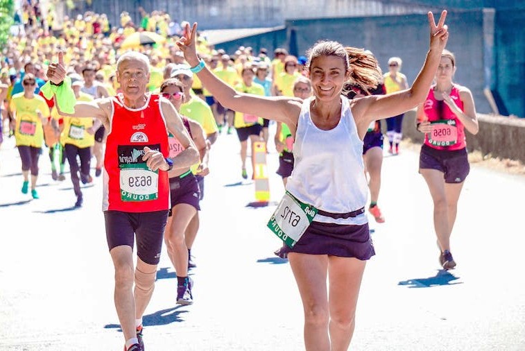 Runners in a community road race on a sunny street, with two participants smiling in the foreground
